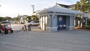 A gated entrance with a blue door, a golf cart, and a parking area with cars. - Steps to the beach.  Pet friendly Beach House w/pool!  4 Bedrooms sleeps 12! (North Myrtle Beach)