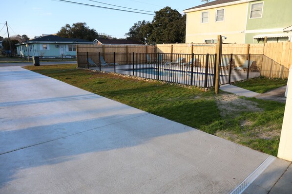 Un barrio residencial con entrada de hormigón, patio trasero cercado y casas al fondo.