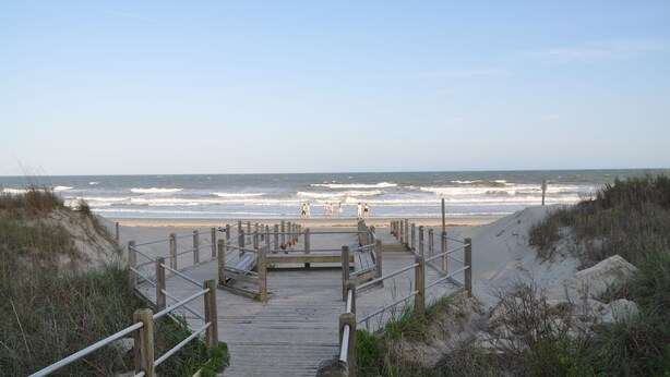 A wooden boardwalk leading to a beach with waves crashing onto the shore. - Steps to the beach.  Pet friendly Beach House w/pool!  4 Bedrooms sleeps 12! (North Myrtle Beach)