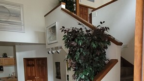 A spacious living area with a dining table and chairs, a staircase with wooden railings, and a potted plant. - 3500 Sq Ft Home 4 Suites Pool Table, Hot Tub, Bikes, EV Charger, 4th Night Free! (Bend)