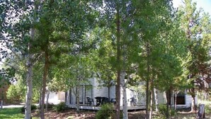 A house with a porch, surrounded by trees and a dog. - 3500 Sq Ft Home 4 Suites Pool Table, Hot Tub, Bikes, EV Charger, 4th Night Free! (Bend)