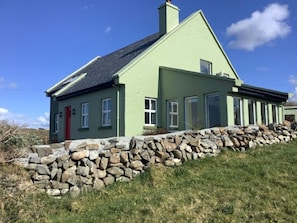 A two-story house with a stone wall in front, a red door, and a sloped roof. - A Unique Cottage, Doolin  Breathtaking Ocean & Burren views            (Doolin)
