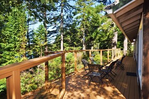 Eine Holzterrasse mit Glastisch und Stühlen, umgeben von dichtem Wald.