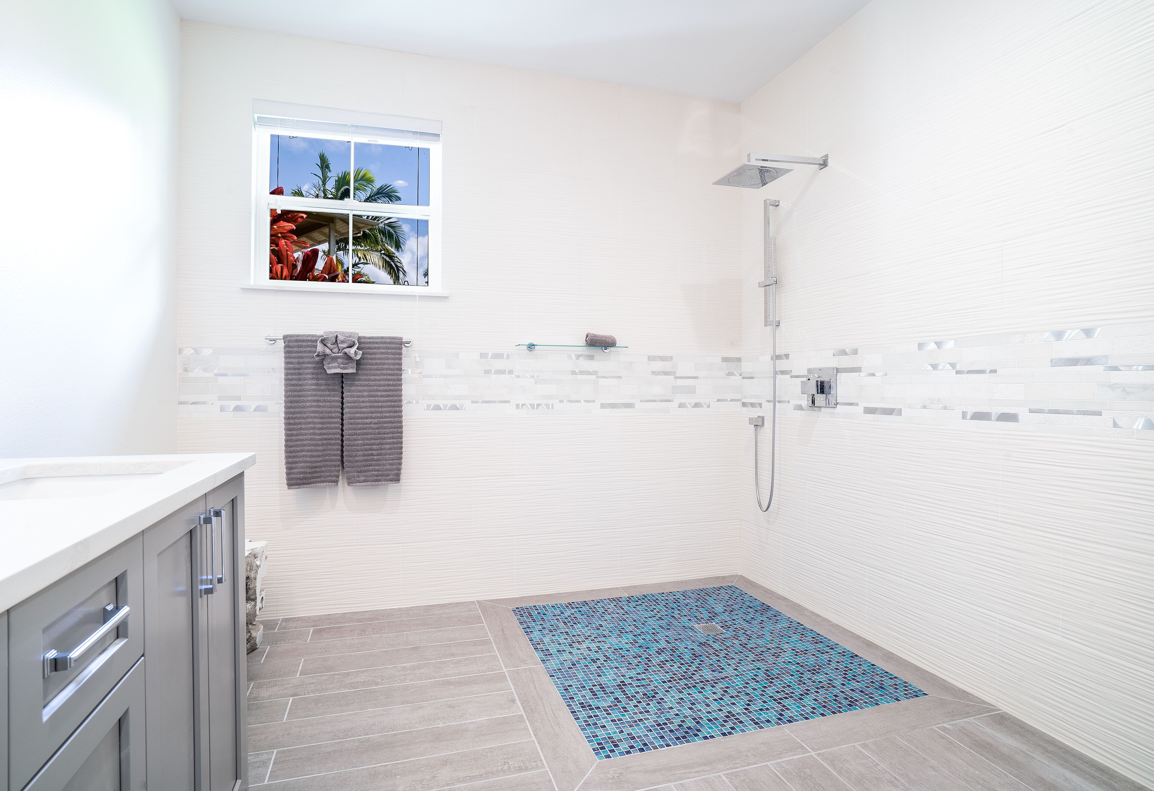 Une salle de bain moderne avec une douche, une fenêtre donnant sur des palmiers et un sol carrelé.