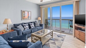 Un salon comprenant un canapé, une table basse et un téléviseur, un ventilateur de plafond et un balcon avec vue sur l’océan.