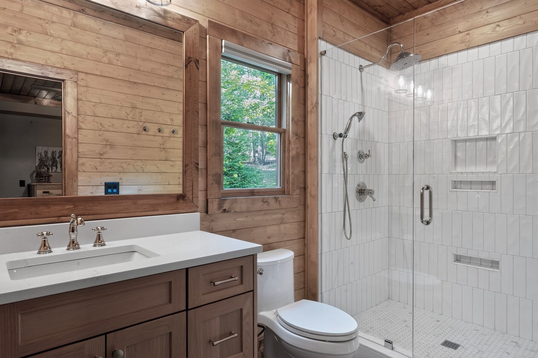 A bathroom with a wooden vanity, a toilet, and a glass-enclosed shower.