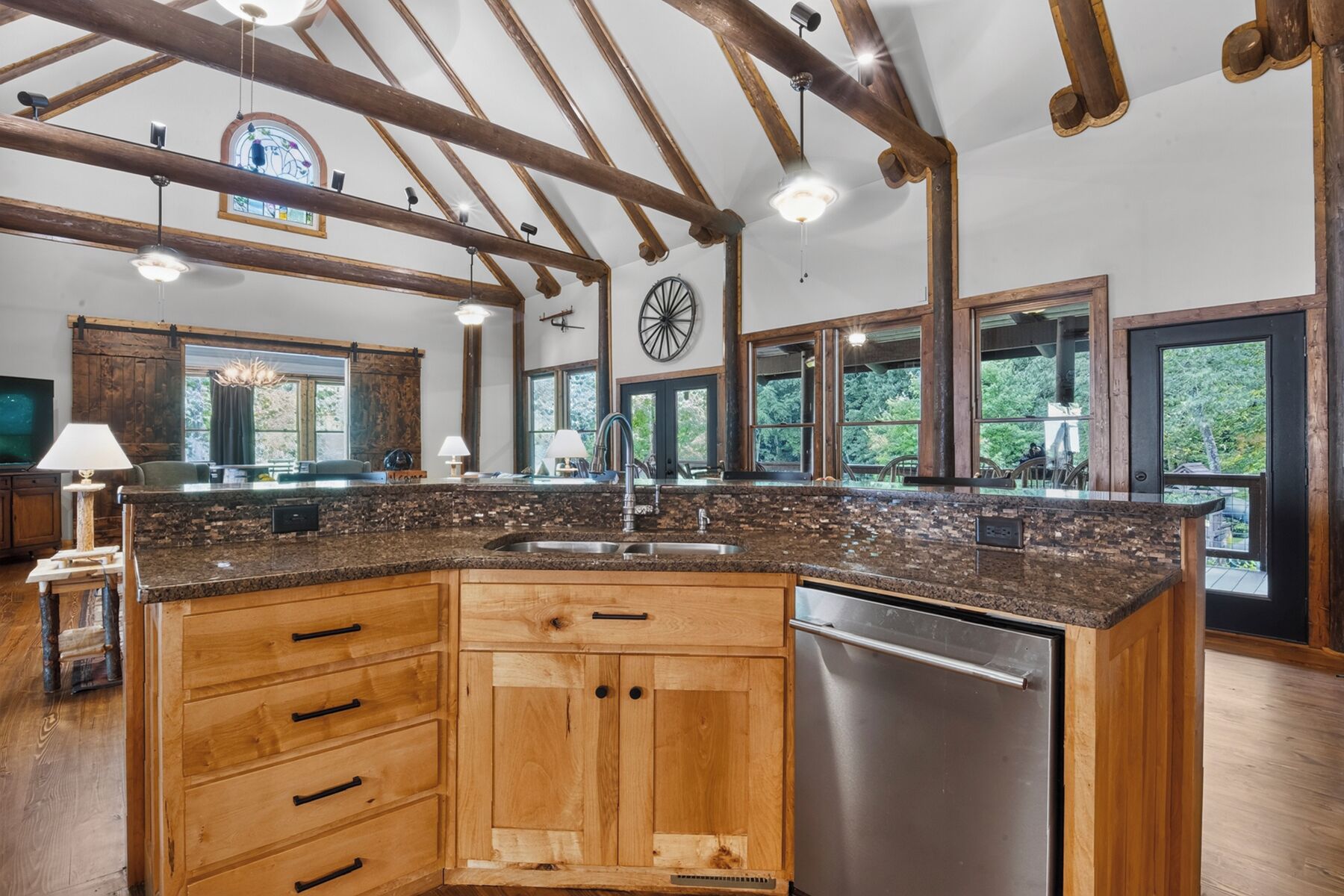 A spacious kitchen with wooden cabinets, a stainless steel dishwasher, and large windows offering views of the outdoors.