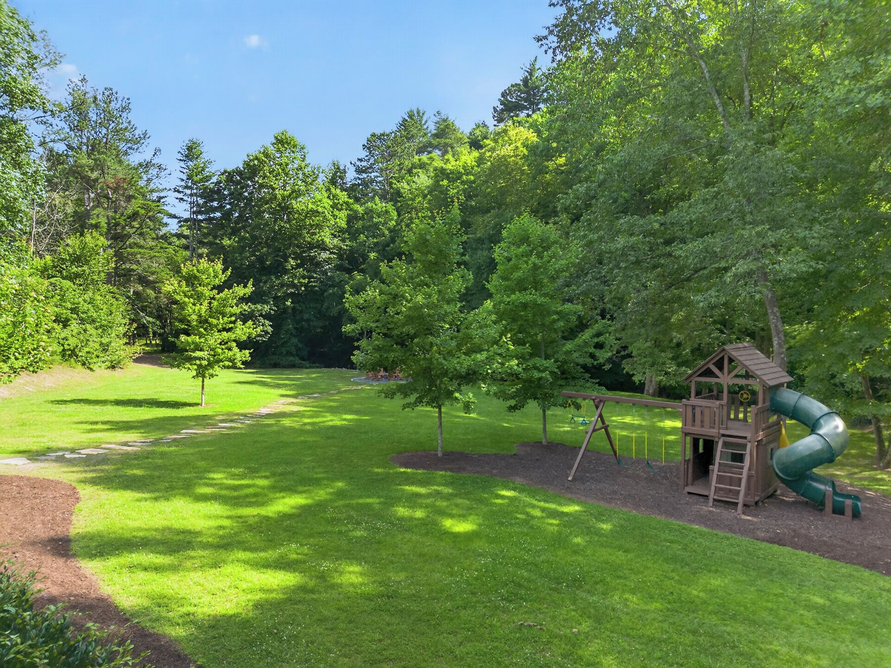 Een speeltuin met glijbaan, schommel en klimrek, omgeven door bomen en gras.