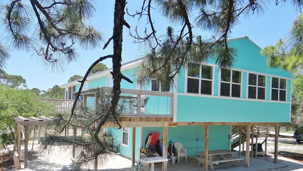 Une maison turquoise à deux étages, dotée d’un balcon, d’un espace salon extérieur et d’un coin barbecue.