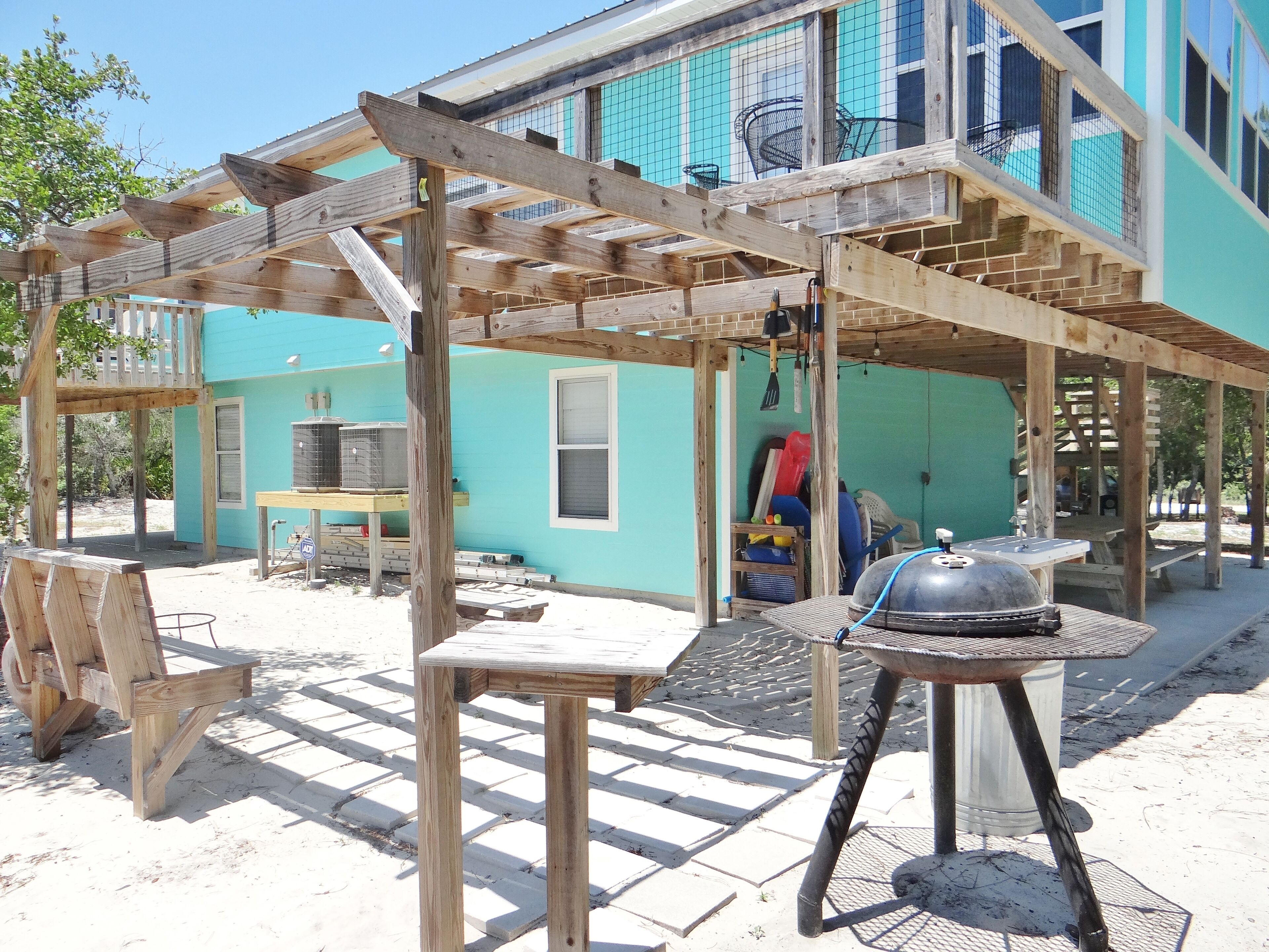 Een houten pergola met een barbecue en vogelkooien in een achtertuin.