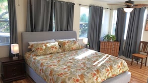 Une chambre à coucher avec un grand lit, des rideaux gris, une commode en bois, une chaise et un ventilateur de plafond.