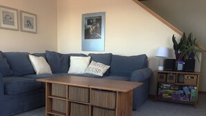 A living room with a blue sofa, a wooden coffee table, and a bookshelf with board games. - Direct access to the beach! (Plymouth)