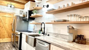 A modern kitchen with stainless steel appliances, wooden shelves, and a marble countertop.