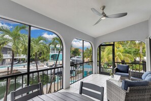 A balcony with a view of a pool, palm trees, and a boat.