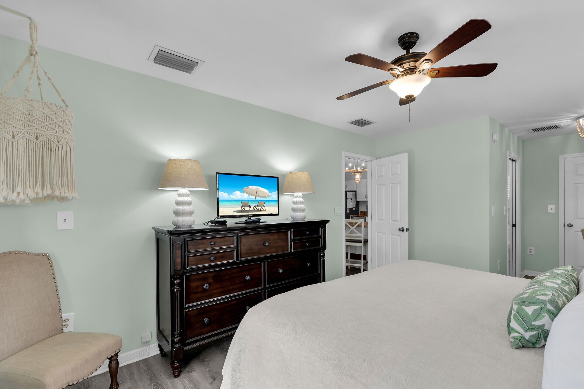 A bedroom with a bed, a dresser, a television, and a ceiling fan.
