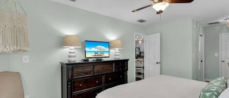 A bedroom with a bed, a dresser, a television, and a ceiling fan.