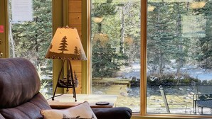 Een gezellig cabin interieur met een groot raam dat uitzicht biedt op een bos en een beek.