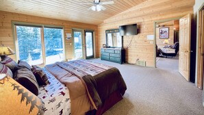 Een ruime slaapkamer met een groot bed, een dressoir, een televisie en een plafondventilator.