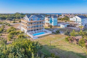 A multi-story residential building with a pool, surrounded by greenery and a clear view of the sea.