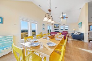 A bright dining area with yellow chairs, a wooden table set for four, and a view of the outdoors through large windows.