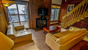 A living room with a stone fireplace, a television, and a staircase.