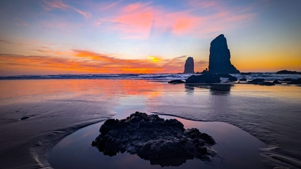 A beach with a rock formation and a sunset.