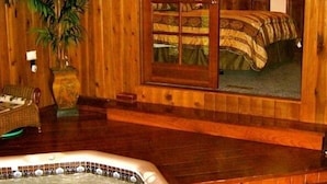 A wooden interior with a hot tub, a large window, and a bed with a striped blanket.