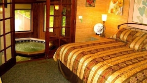 A room with a large bed, a wooden door, a small window, and a wall-mounted lamp.