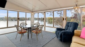 A spacious room with a large window overlooking a lake, a dining table with chairs, and a comfortable seating area with a sofa and armchair. - West Bend Lake House-Sleeps 12- Pontoon Avail-Full Pickleball & Basketball Court (West Bend)