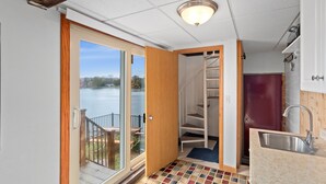 A compact kitchen with a built-in sink, a wooden door leading to a balcony, and a view of a lake. - West Bend Lake House-Sleeps 12- Pontoon Avail-Full Pickleball & Basketball Court (West Bend)