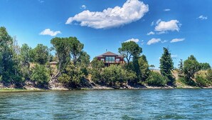 Una casa junto a un lago, con cielo despejado y árboles circundantes.
