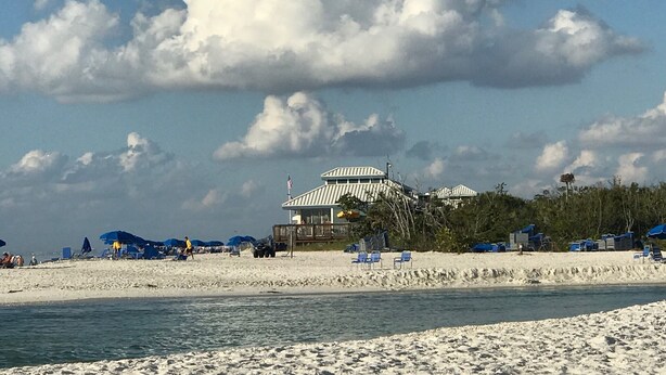 Een strand met een groot gebouw, parasols en ligstoelen.
