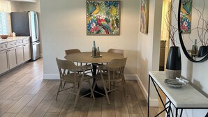 Een moderne keuken met een eethoek, houten vloeren en een groot schilderij van tropische vogels.