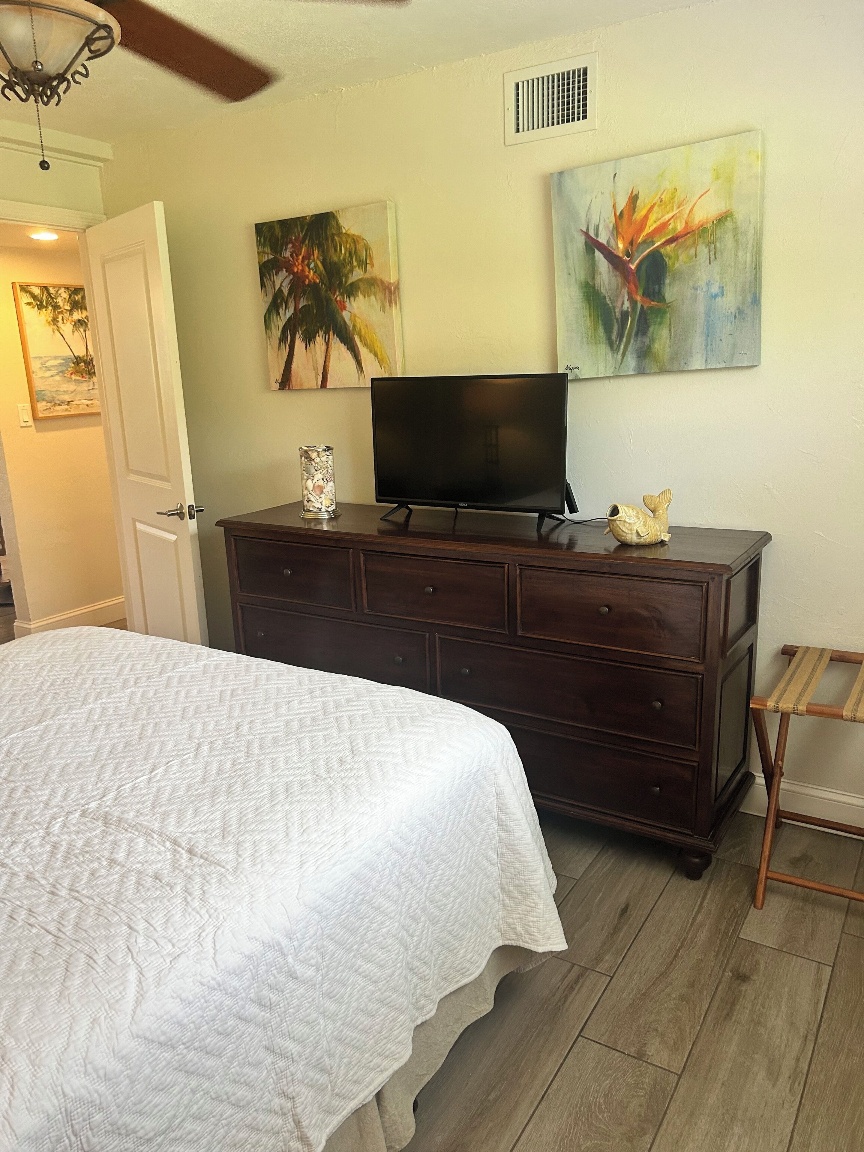 A bedroom with a bed, dresser, TV, and artwork on the wall.