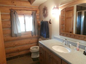 Baño de cabaña de madera con inodoro, lavamanos y ventana con cortinas.