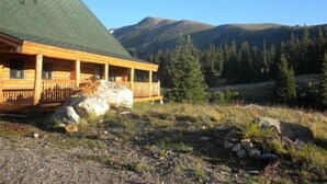 A log cabin with a green roof, wooden deck, and a view of mountains and pine trees. - Exclusive 23-Acre Rocky Mtn. Retreat - Featured in a Music Video!  Unforgettable (Fairplay)