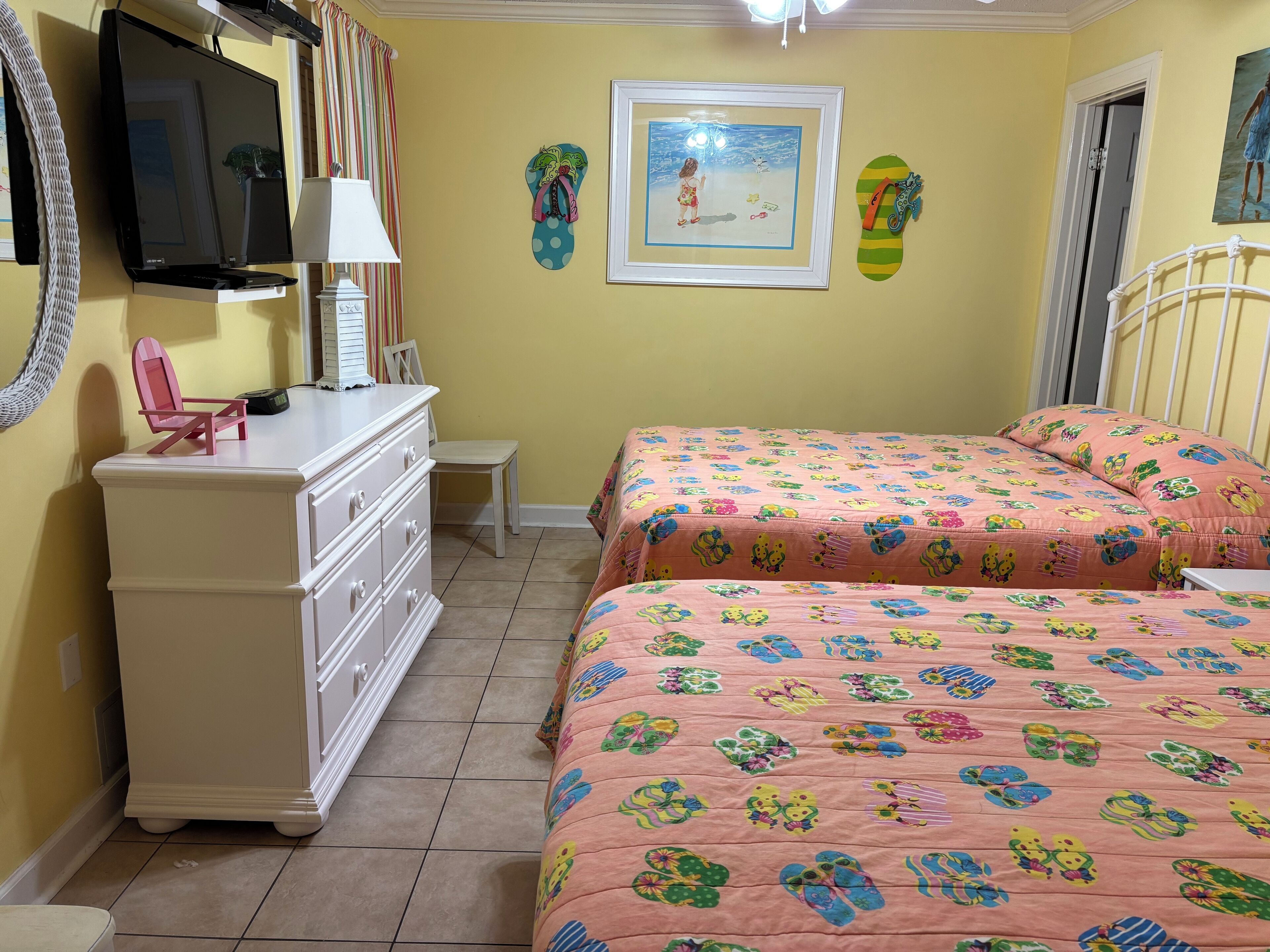 Une chambre avec deux lits, une commode, un téléviseur et un tableau encadré au mur.