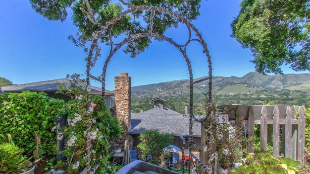 A stone archway leading to a house with a stone chimney, surrounded by lush greenery and a mountainous backdrop. - Carmel Valley Village, close to Big Sur, Pebble, Carmel, & Monterey (Carmel Valley)
