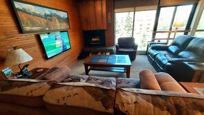 A cozy living room with a fireplace, leather sofa, and a television mounted on the wall. - Ski-In/Ski-out  - 50 ft from SuperBee Lift (Copper Mountain)