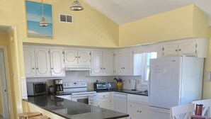 Cozinha com armários brancos, uma ilha central com banquetas, uma geladeira e um micro-ondas.