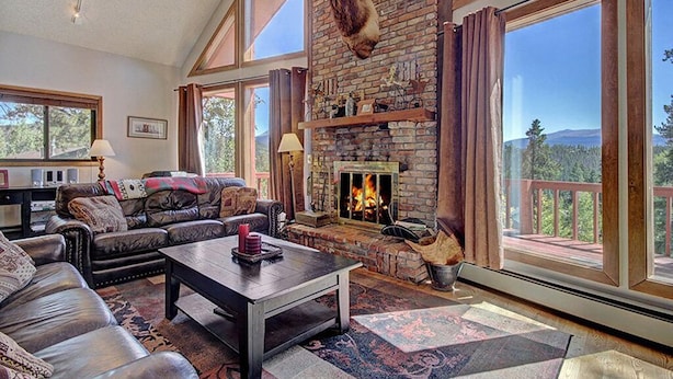 Amplia sala de estar con chimenea, muebles de cuero y grandes ventanas que ofrecen vistas al exterior.