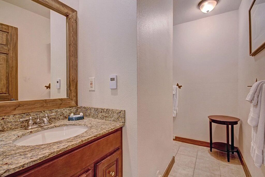 A bathroom with a granite countertop sink, wooden vanity, and a large mirror.