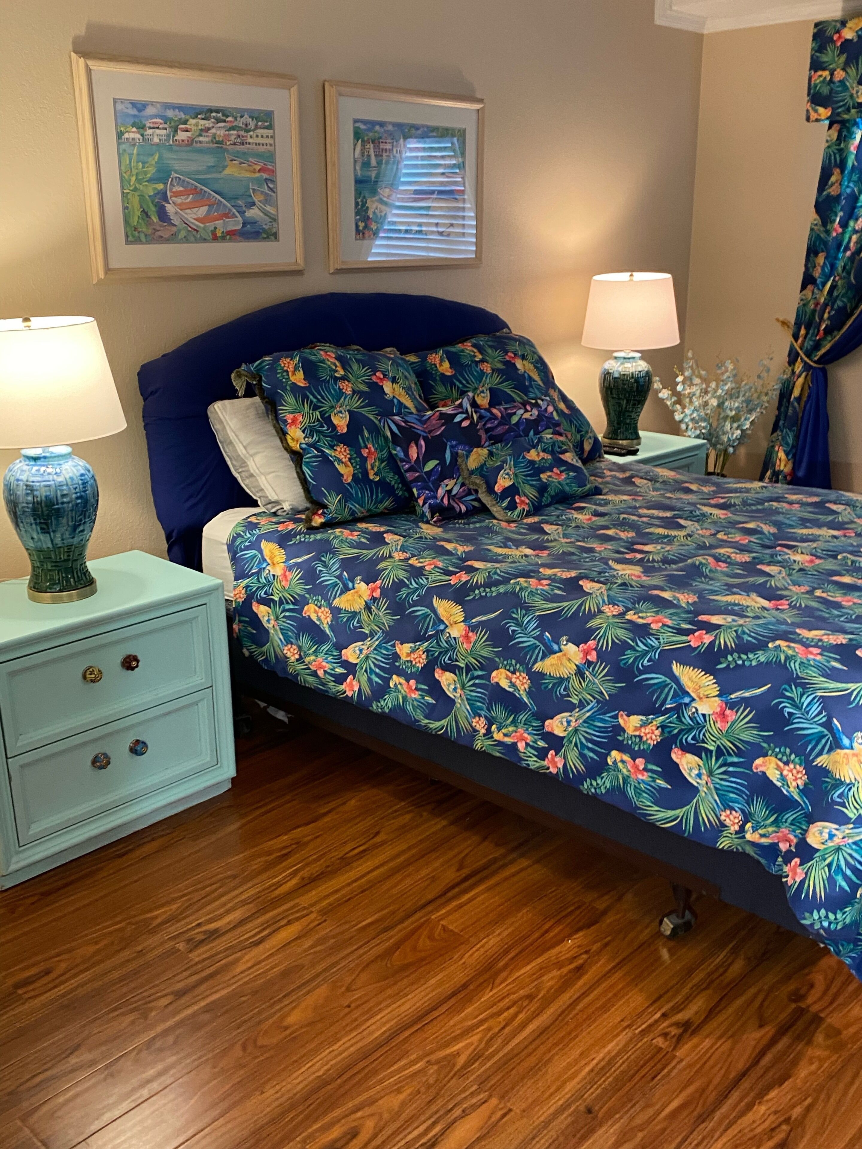 A bedroom with a bed, two nightstands, a blue headboard, floral bedding, and two wall-mounted paintings.