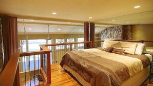 Ein Schlafzimmer mit einem großen Bett, Holzboden, einem Balkon mit Geländer und einer Steinwand.