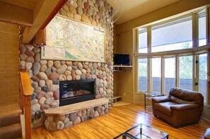 Un salón con chimenea de piedra, un mapa en la pared, un sofá de cuero y ventanas amplias.