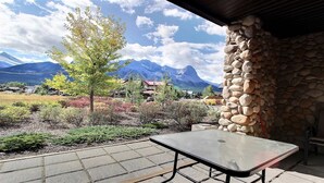 Une terrasse avec une table et des chaises, un mur en pierre et une vue sur les montagnes et les maisons.