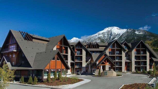 Un chalet moderne au design symétrique, doté de nombreux balcons et de grandes fenêtres, qui se dresse sur fond de montagnes enneigées.