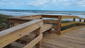 A wooden boardwalk leading to a beach with waves in the background.