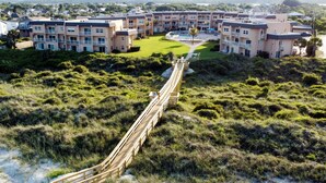 A coastal hotel with a wooden boardwalk leading to a grassy area and a pool.