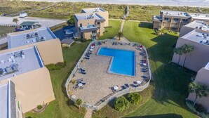 An aerial view of a resort with a central swimming pool, multiple buildings, and a beach view.
